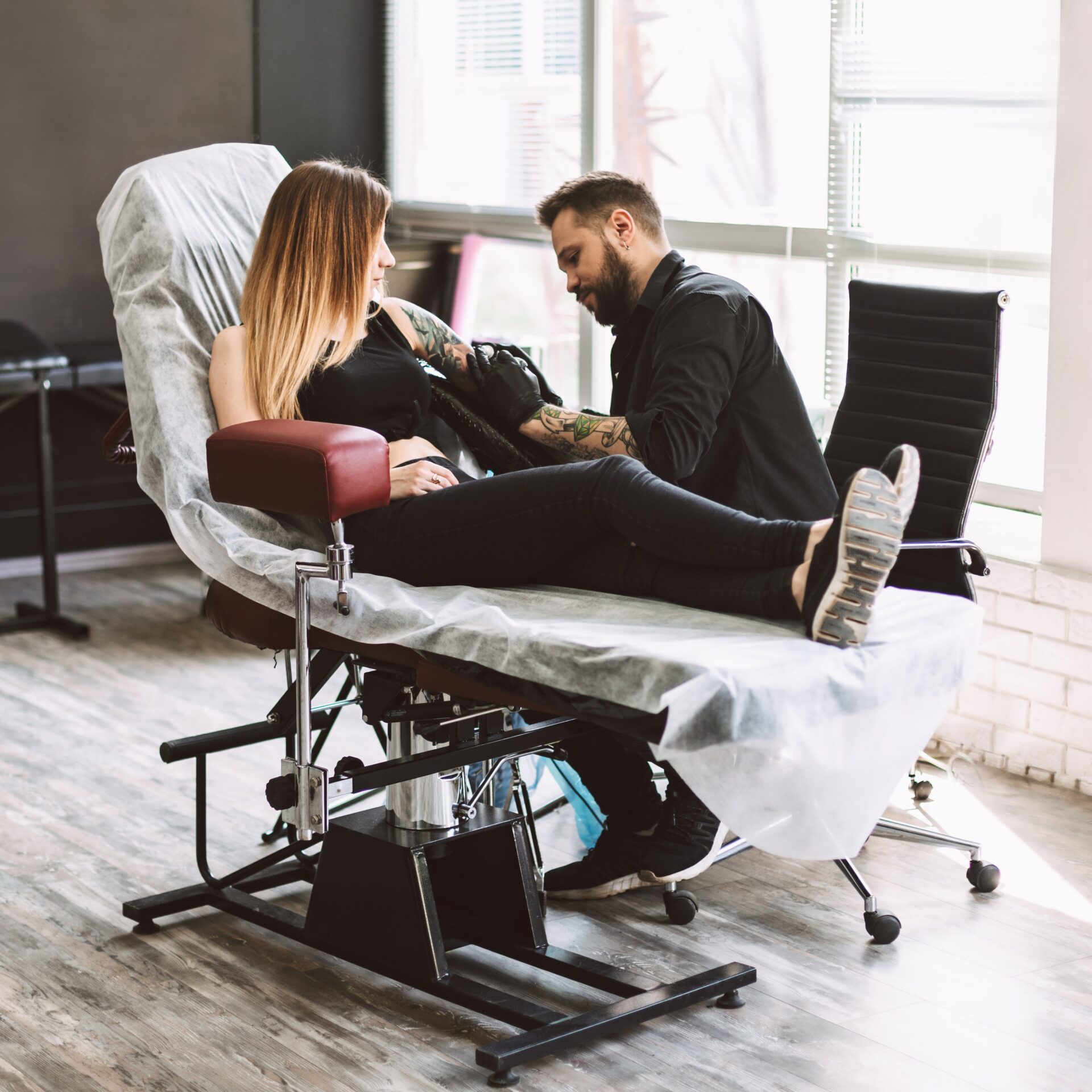 Professional tattooer carefully doing tattoo on girl hand using tattoo machine in modern tattoo studio