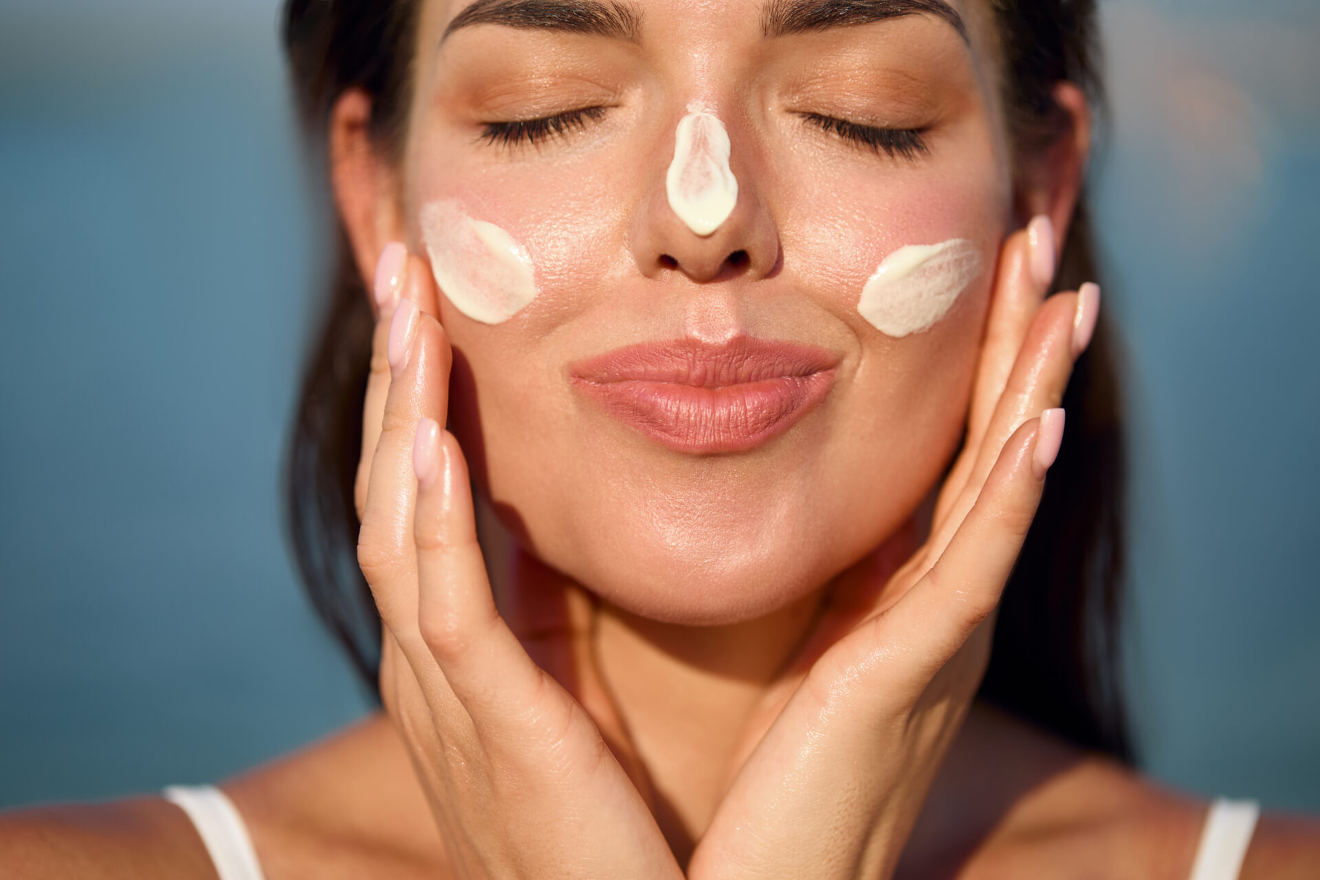 Beautiful young woman with sun cream on face. Girl applying sunscreen lotion on skin.Skin care. Sun protection. Suntan woman with sunscreen on her face